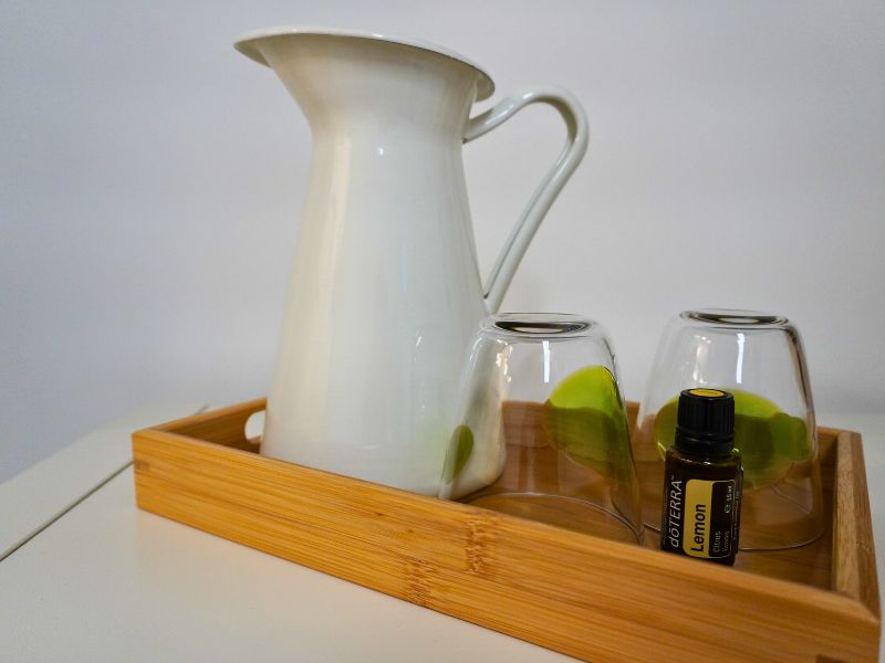 Weißer Wasserkrug, Gläser und ätherisches Zitronenöl auf einem Holztablett
